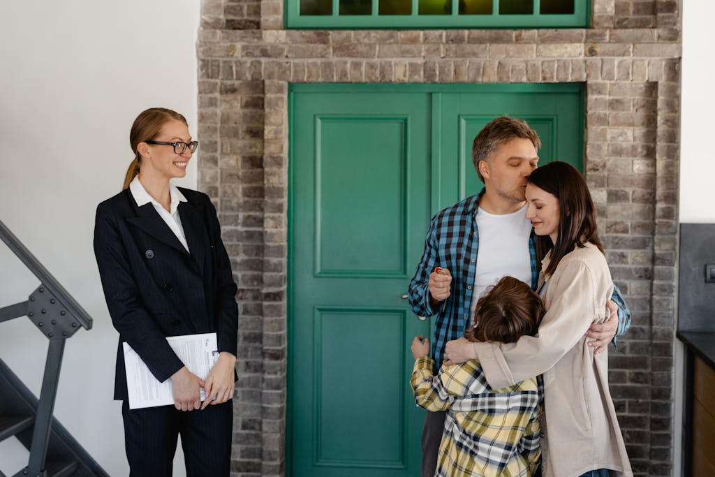 A joyful family embraces in their new home while a smiling realtor stands nearby.