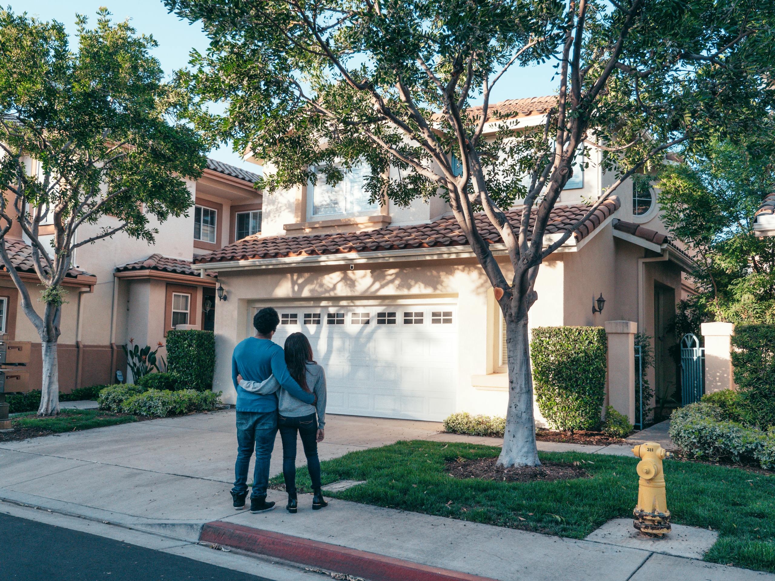 Couple hugging outside their newly purchased suburban home, showcasing togetherness and new beginnings.