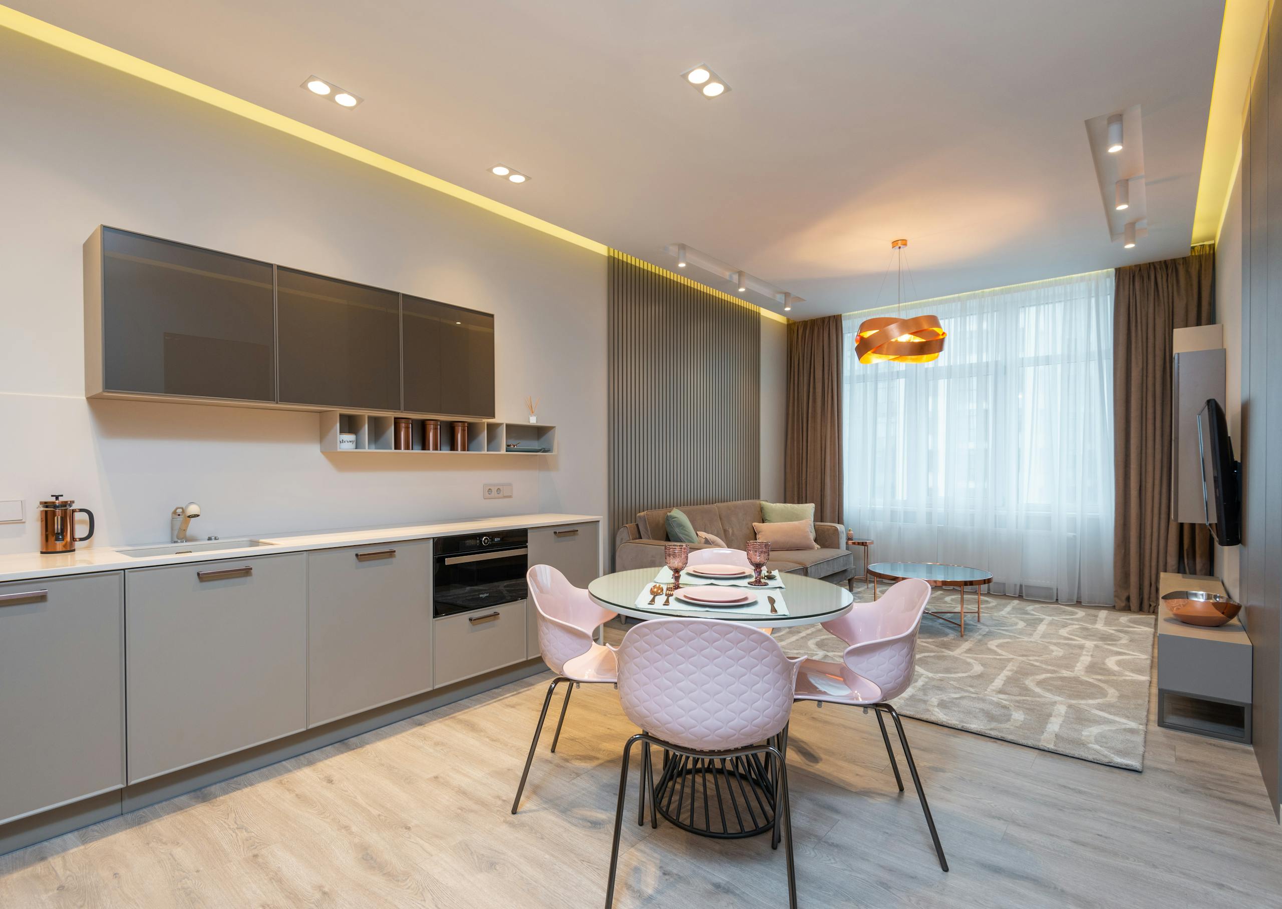 Modern living room with cozy sofa near stylish kitchen zone and round glass dining table