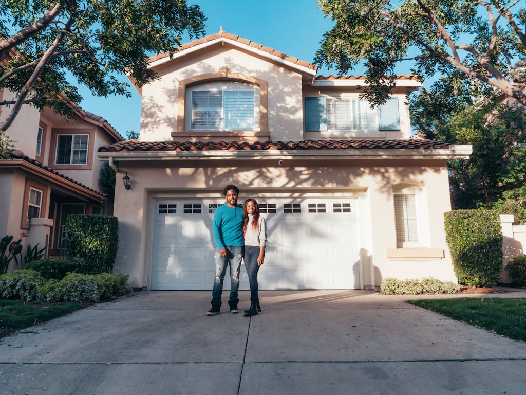 Smiling couple standing outside their newly purchased house on a sunny day.