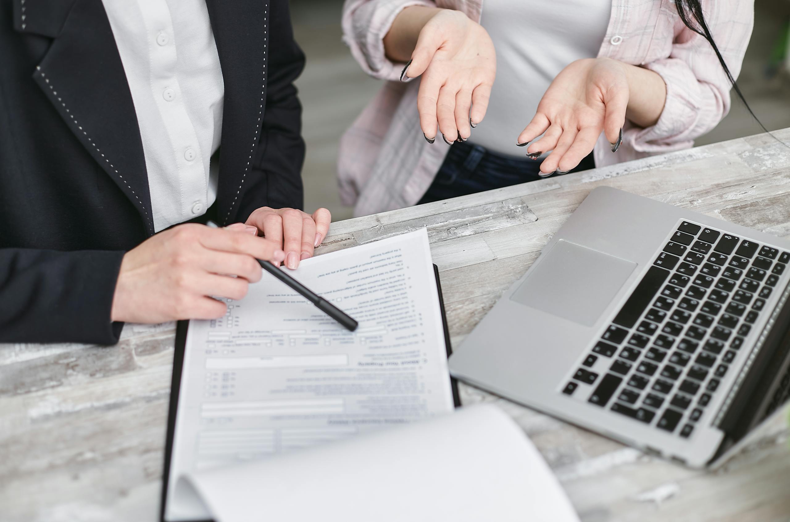 Two professionals discussing a contract at a business meeting with documents and a laptop.